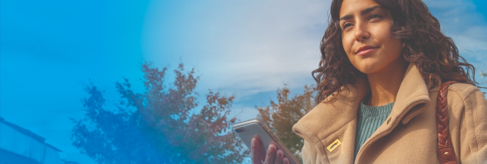 women wearing a coat holding her phone with a thoughtful expression on her face